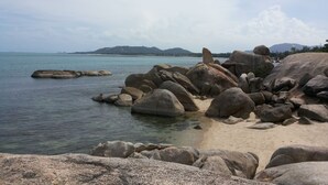 A rocky shoreline with large boulders and calm water. - ASTROCOCO beach resort by Coconut Beach (Koh Samui)