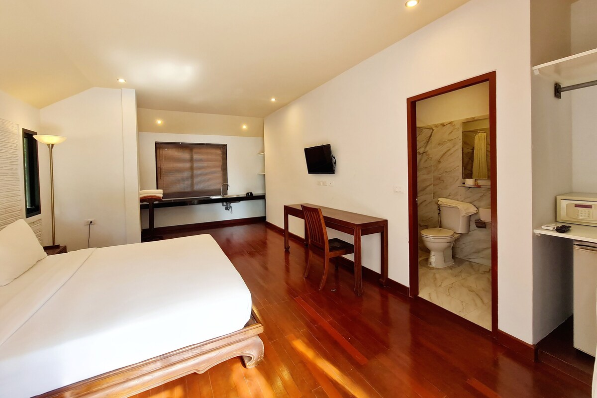 A hotel room with a bed, a desk, a chair, a television, a bathroom, and a marble wall.