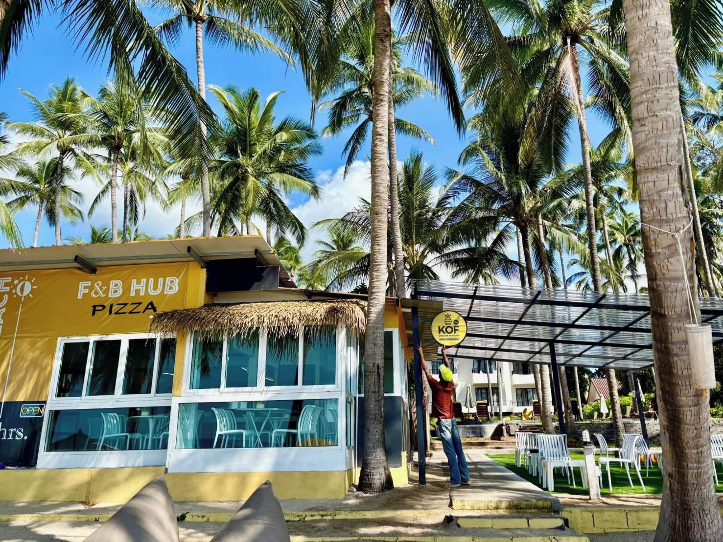 A food establishment named F&B HUB PIZZA with outdoor seating and palm trees in the background.