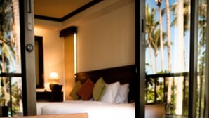 A hotel room with a bed, a wooden table, and a view of palm trees through the window. - ASTROCOCO beach resort by Coconut Beach (Koh Samui)