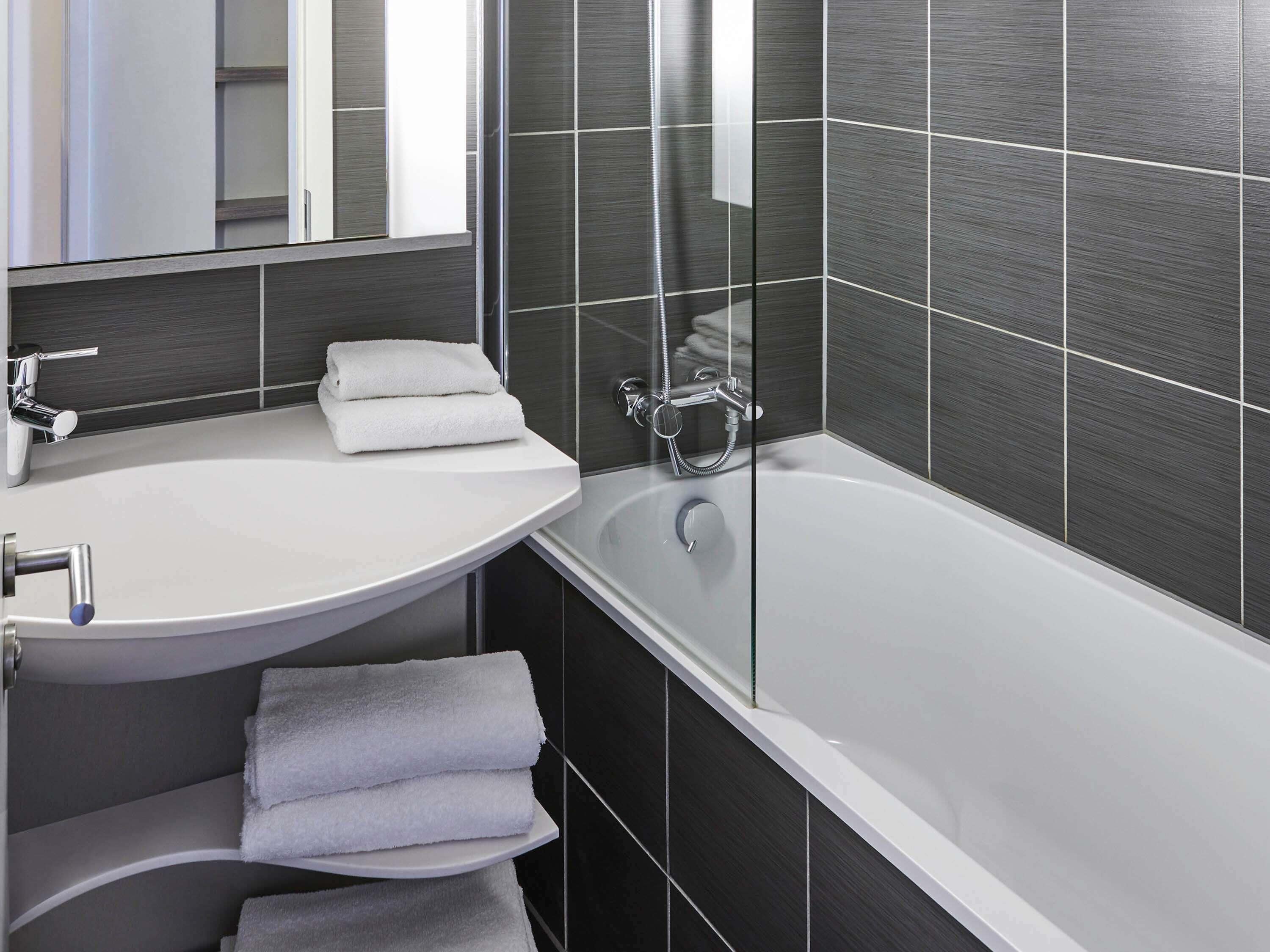 Un bagno moderno con un lavandino bianco, una vasca da bagno e pareti rivestite di piastrelle scure.