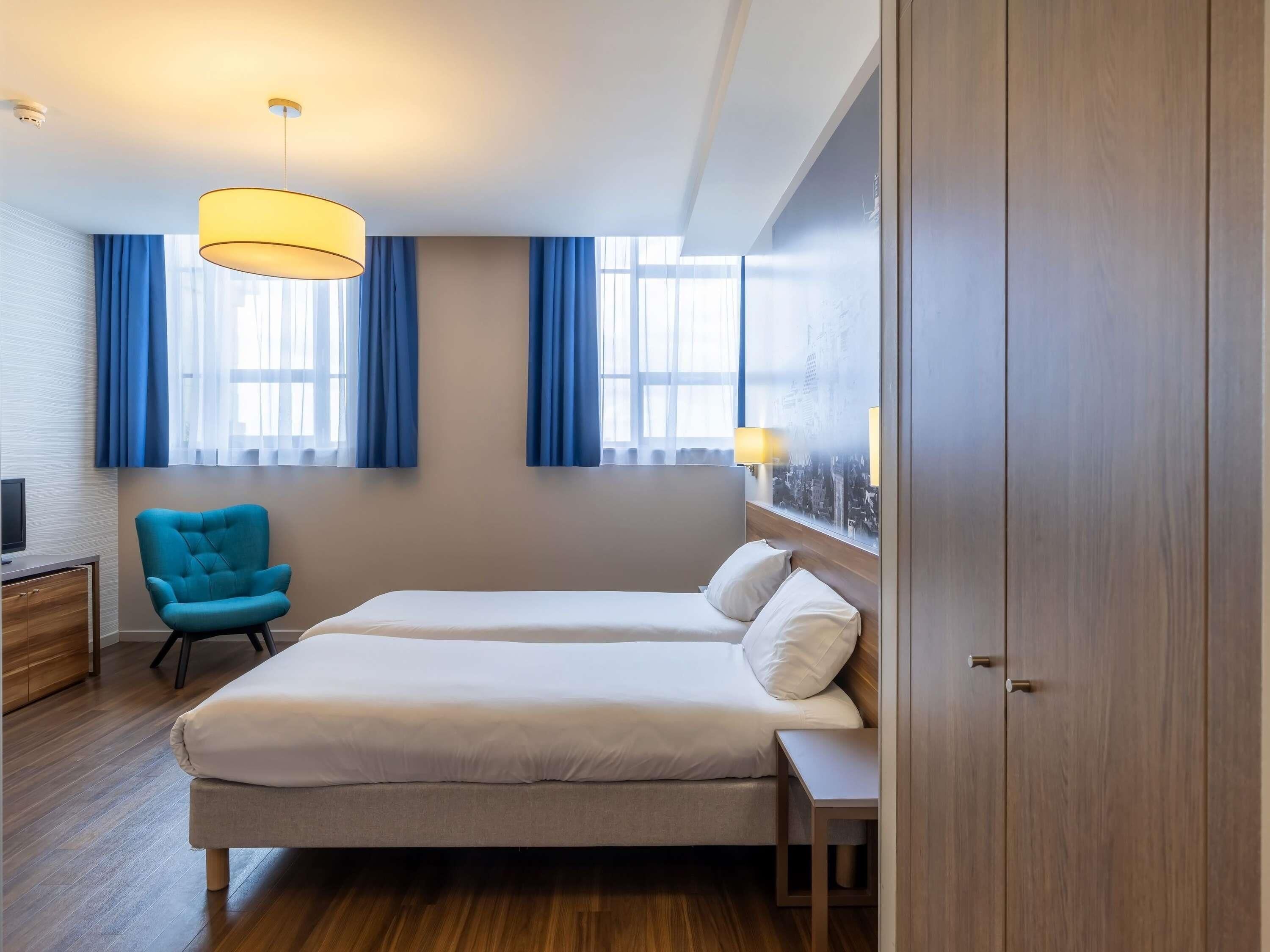 Una habitación de hotel con cama, una silla, un escritorio y un armario.