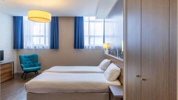 Una habitación de hotel con cama, una silla, un escritorio y un armario.
