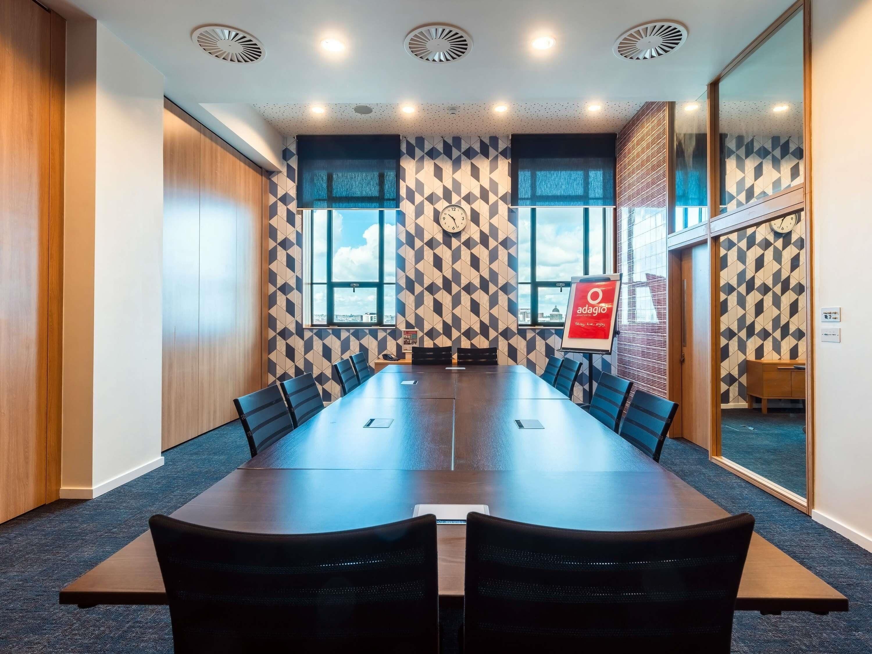 A conference room with a long table, chairs, a clock, and a window with a city view.