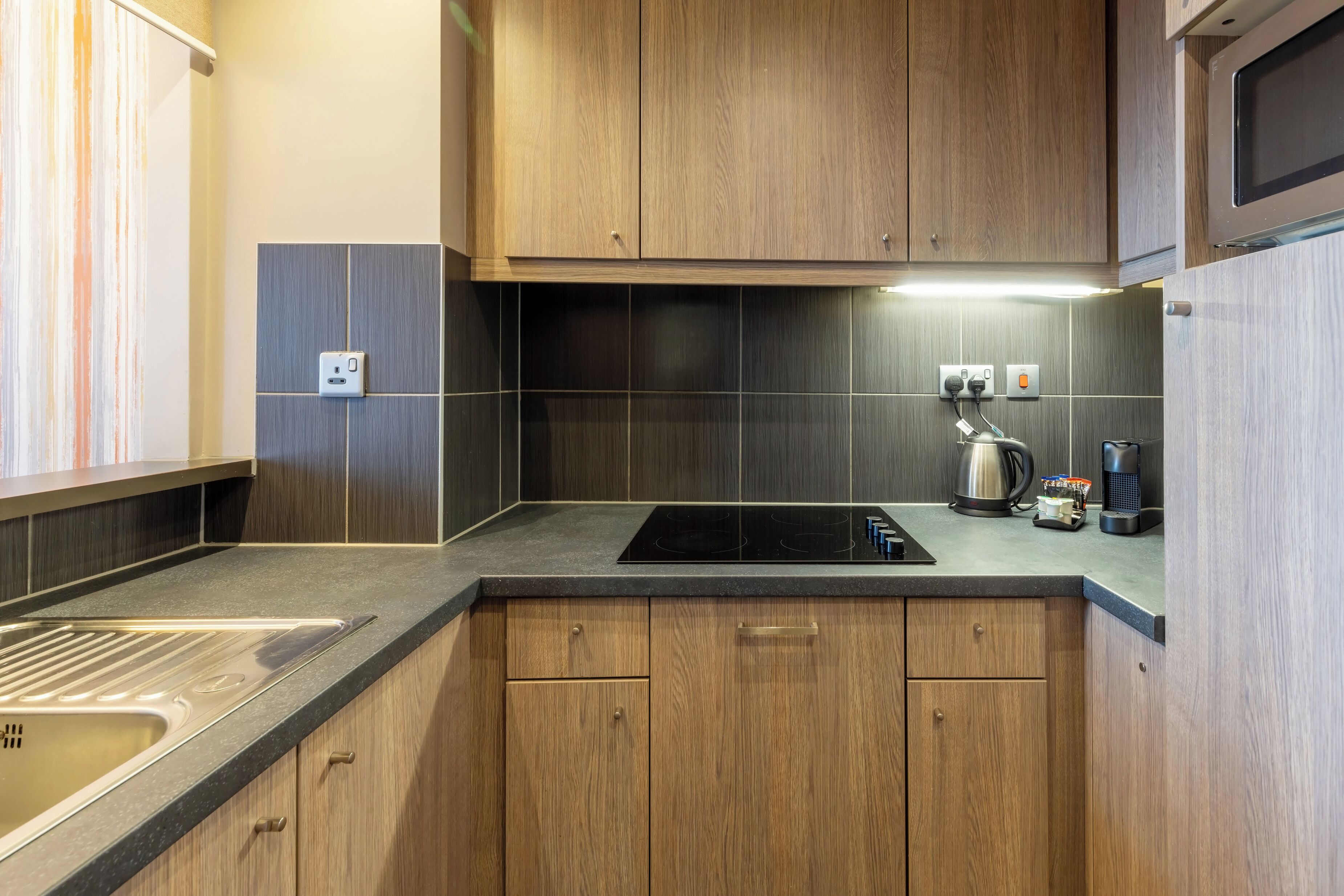 A modern kitchen with wooden cabinets, a black countertop, and a built-in stove.