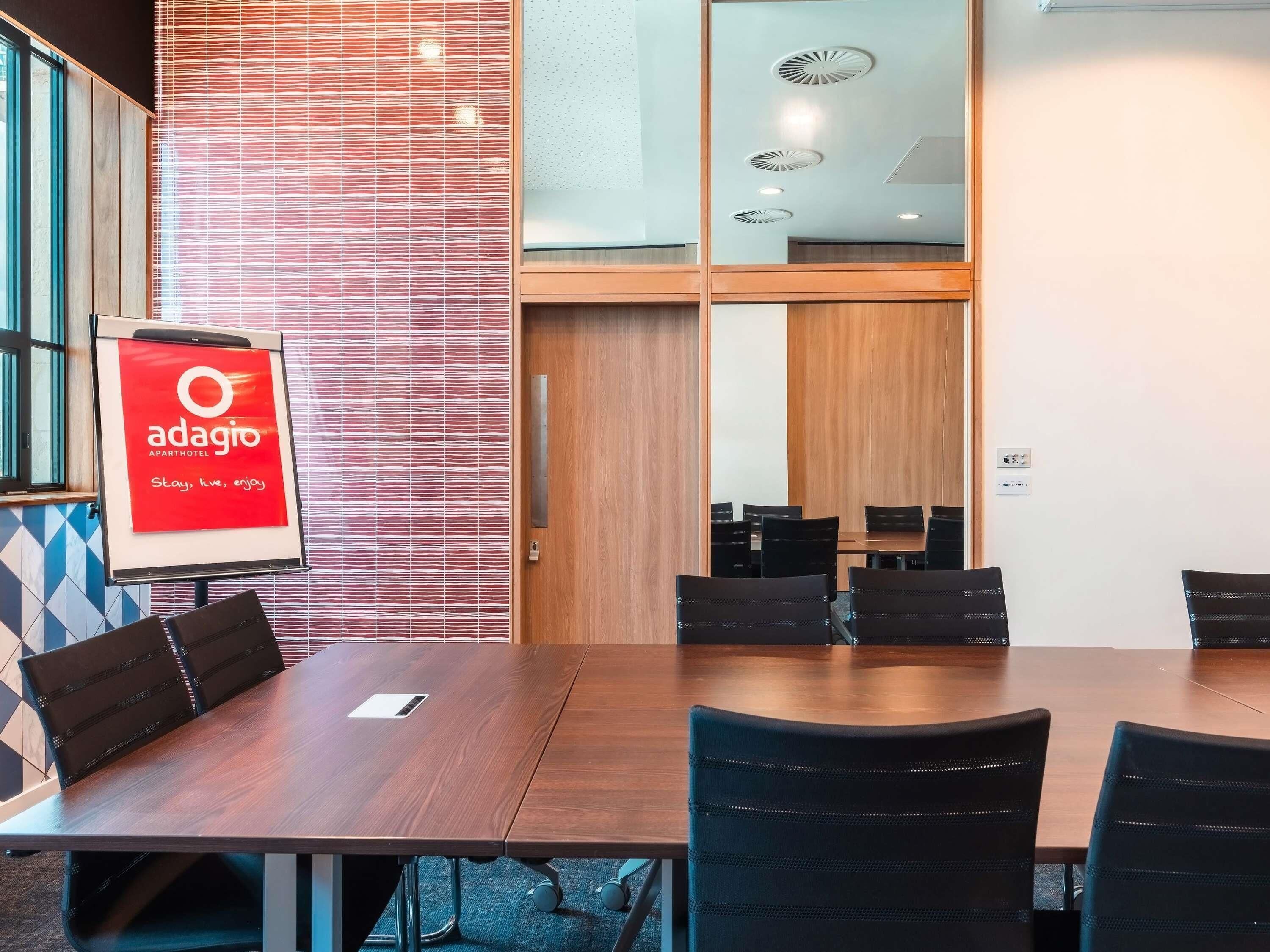 A conference room with a wooden table and chairs, a red sign for Adagio Aparthotel, and a patterned wall.