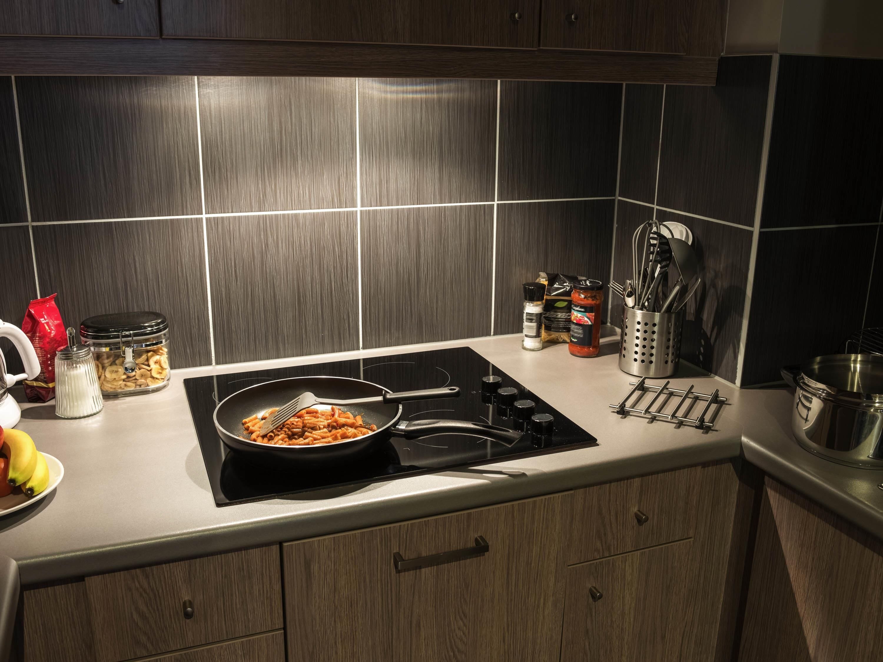 A kitchen with a black induction cooktop, a pan of pasta, a red bag of flour, a jar of sugar, and a container of bananas.