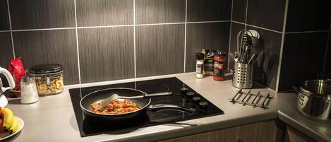 A kitchen with a black induction cooktop, a pan of pasta, a red bag of flour, a jar of sugar, and a container of bananas.