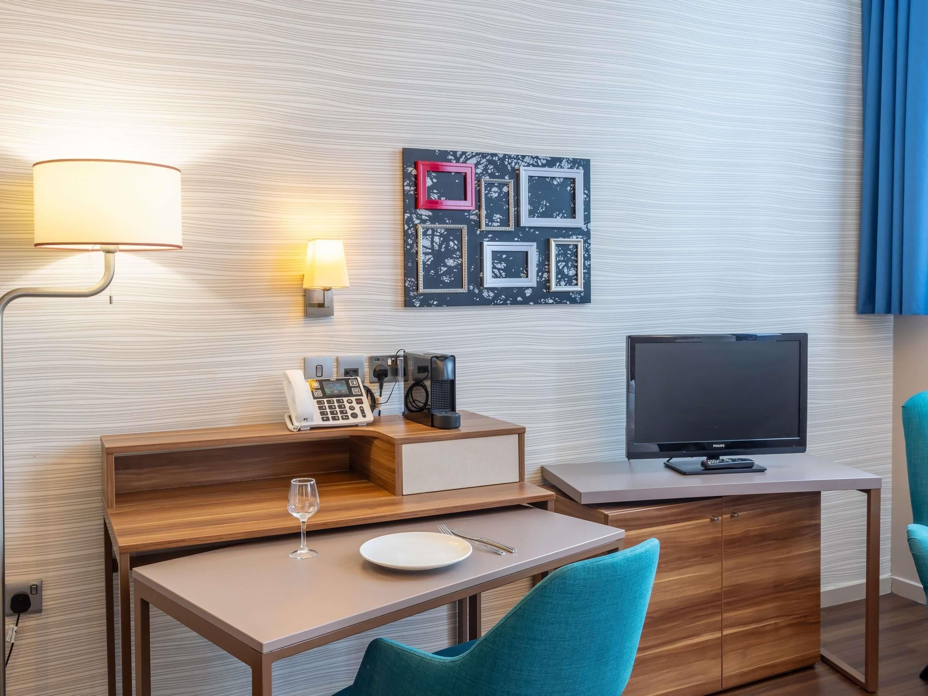 Ein Hotelzimmer mit einem Holztisch, einem Flachbildfernseher, einem Telefon und einer Wandleuchte.
