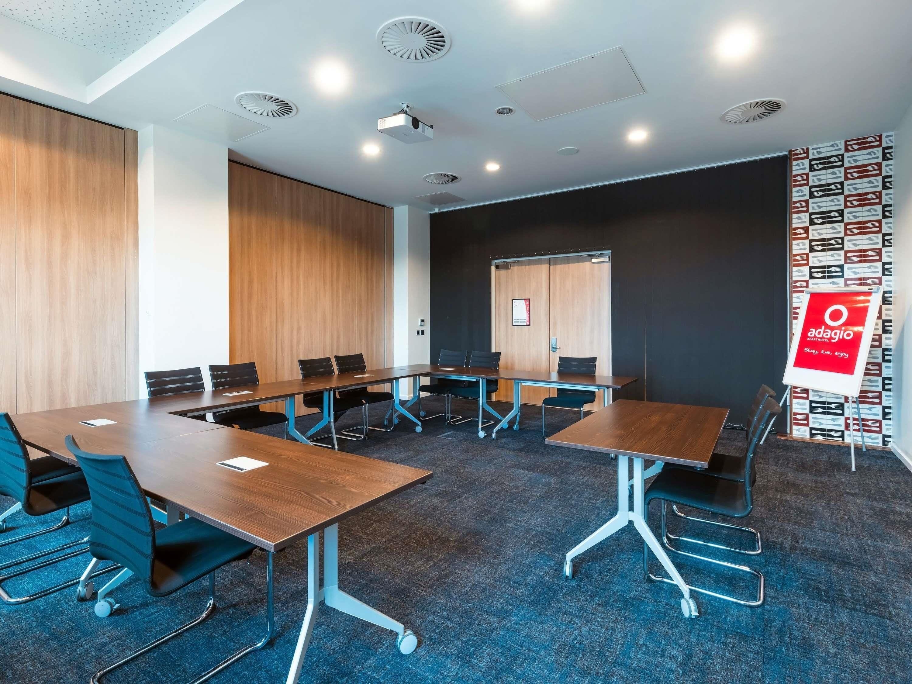 A conference room with a long table, chairs, a projector, and a signboard.