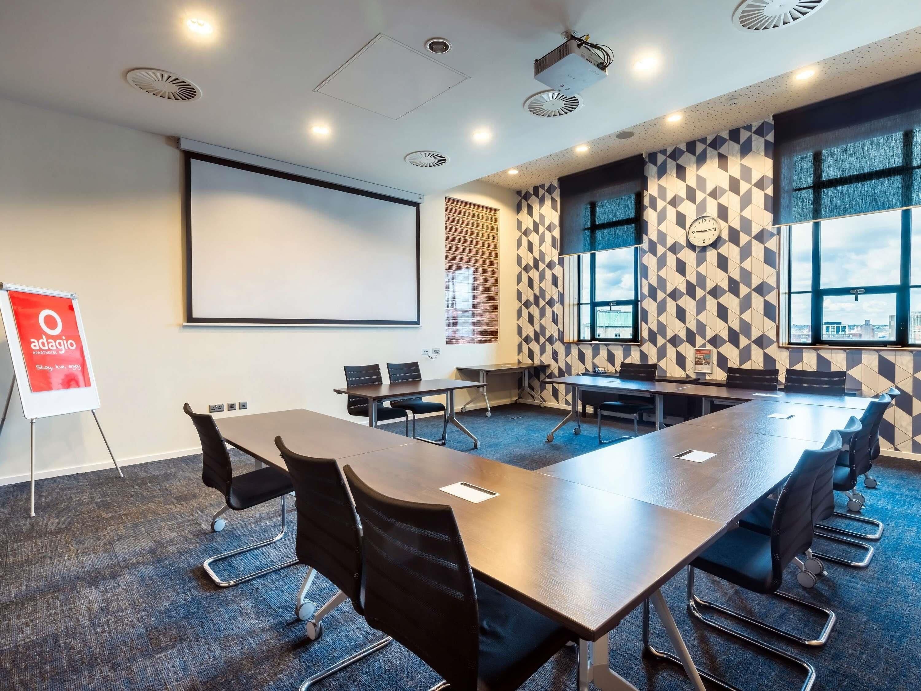 A conference room with a large table, chairs, a projector screen, and a patterned wall.
