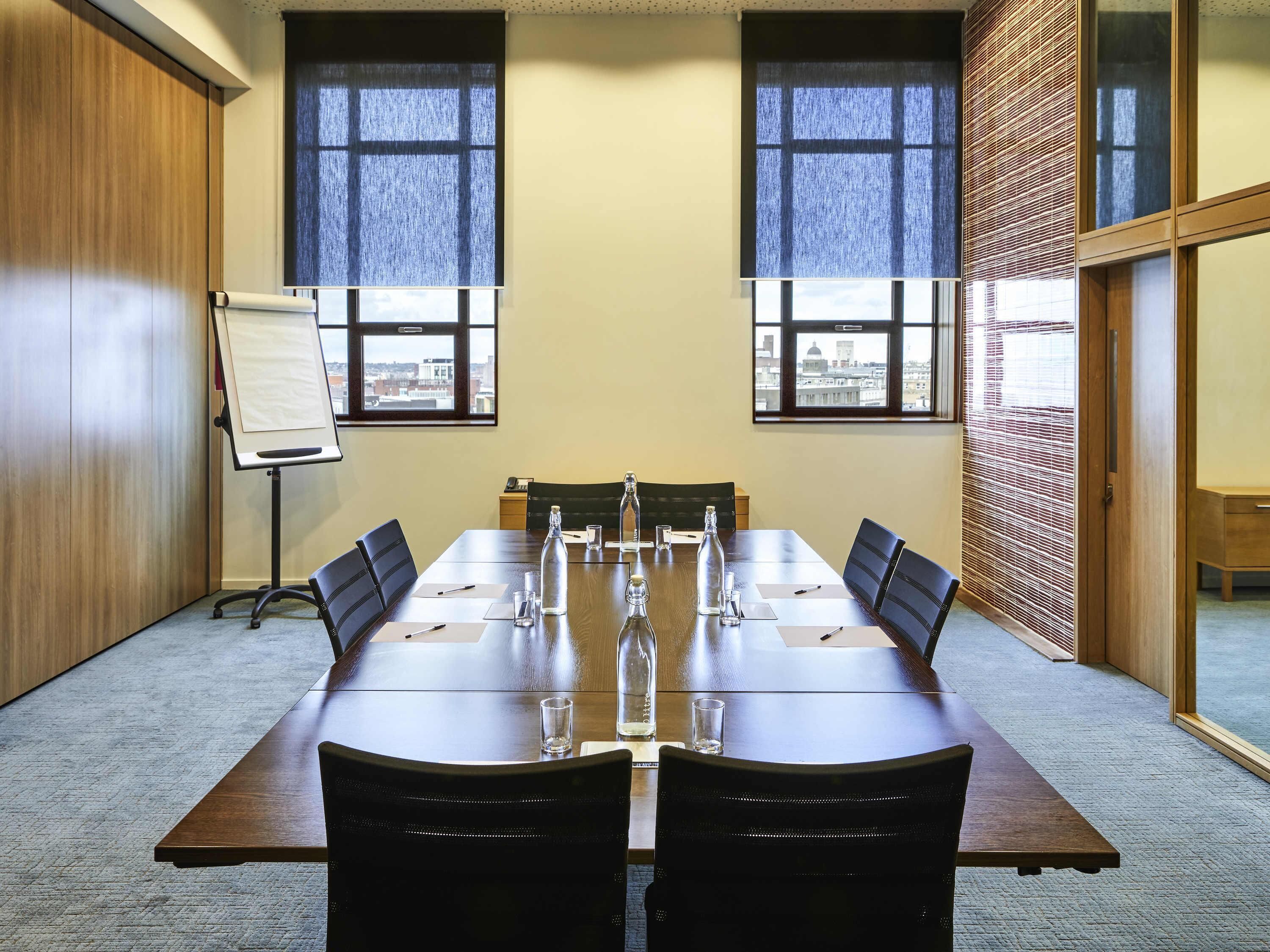 A conference room with a long table, chairs, a whiteboard, and large windows with blinds.