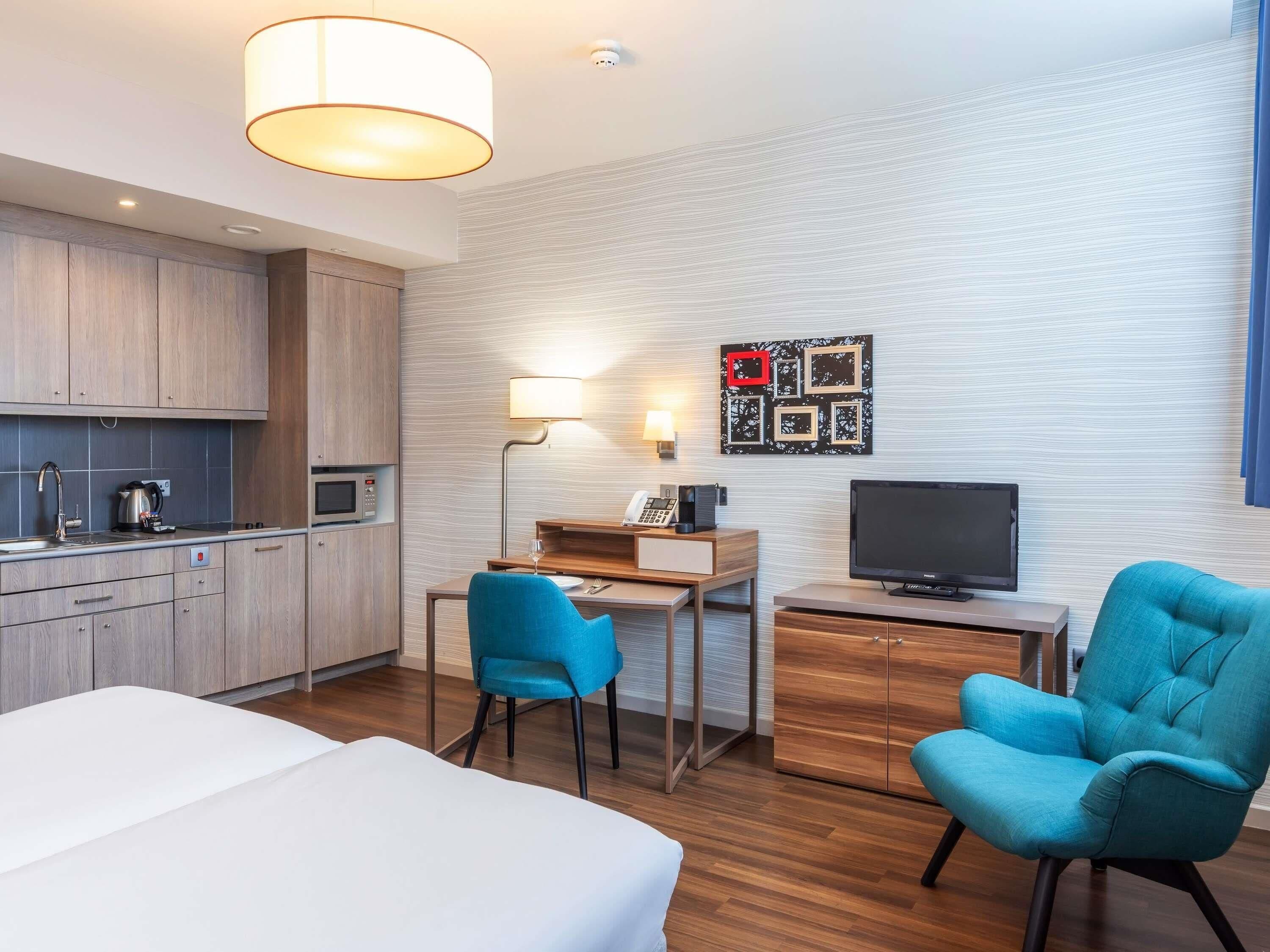 A hotel room with a bed, a desk with a chair, a television, a microwave, and a kitchenette.