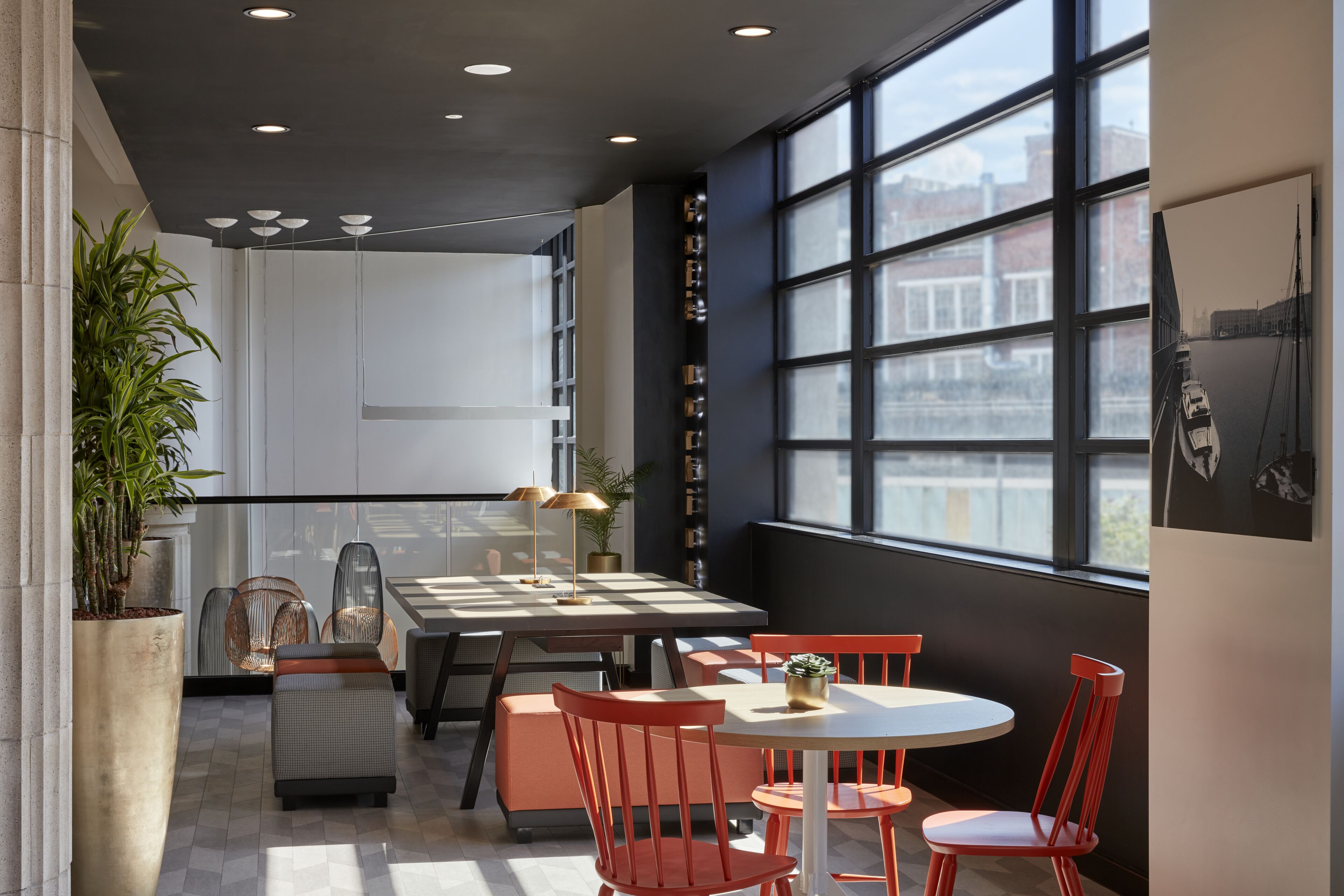 A modern dining area with a large window, a potted plant, and a seating arrangement.
