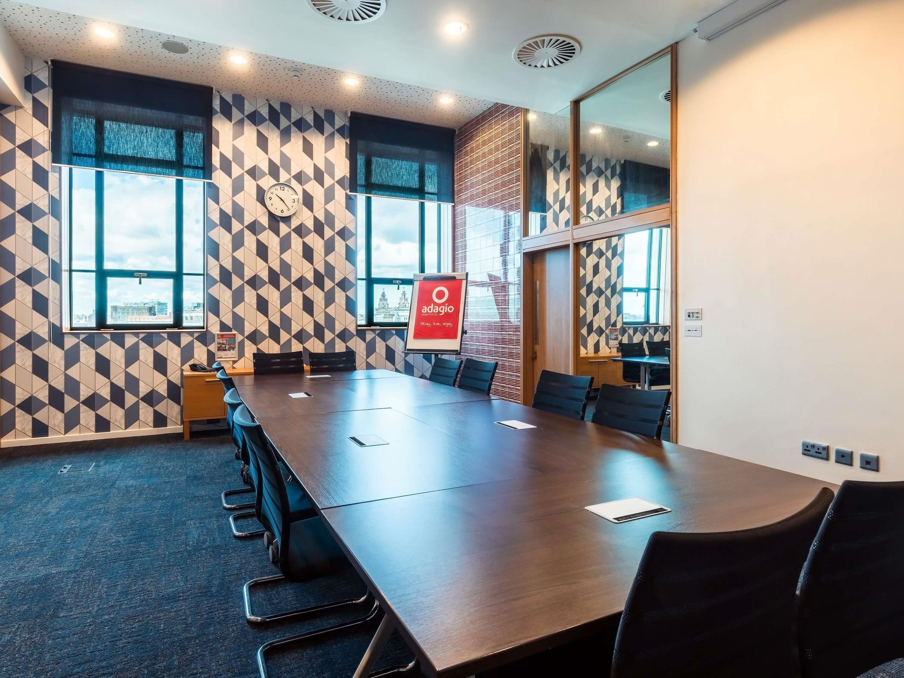 Un salón de conferencias con una larga mesa, sillas y un reloj en la pared.