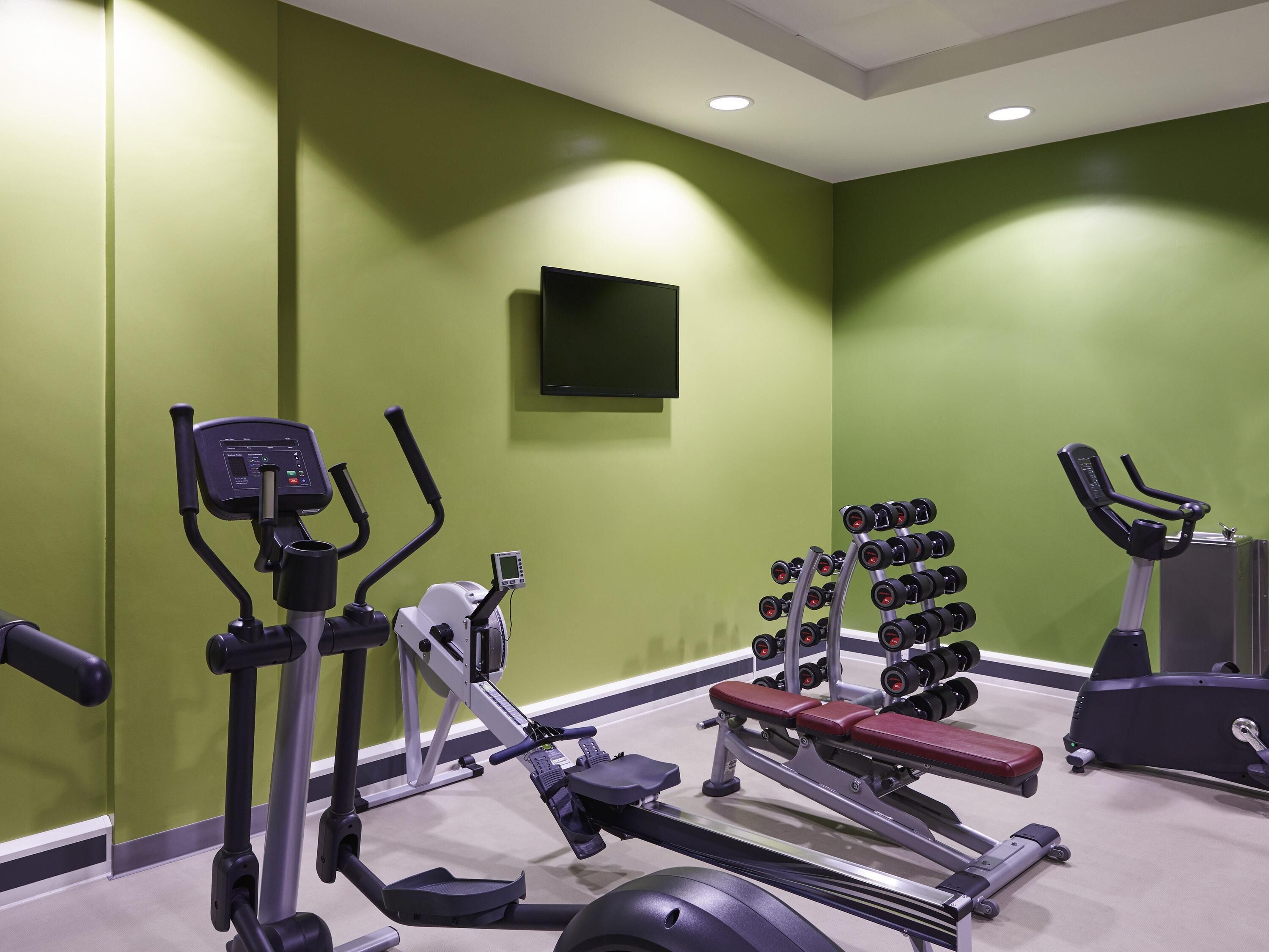 Ett gym med olika typer av träningsutrustning, inklusive löpband, crosstrainer och en viktbänk.