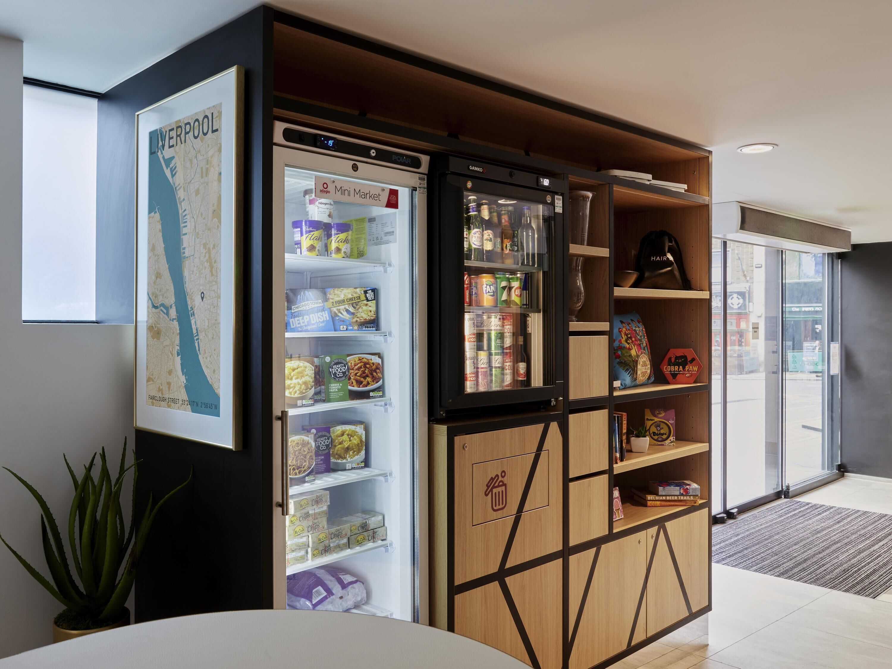 Habitación con un refrigerador pequeño lleno de bocadillos, un mapa de Liverpool y un estante con producto para el cabello.