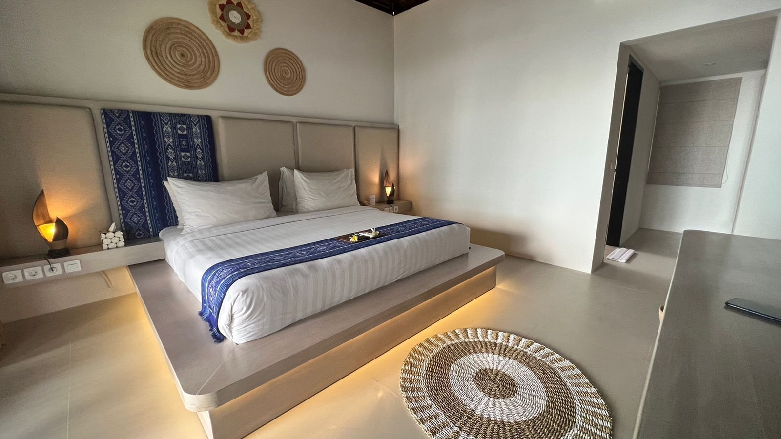 A modern bedroom with a large bed, bedside lamps, and a woven rug.