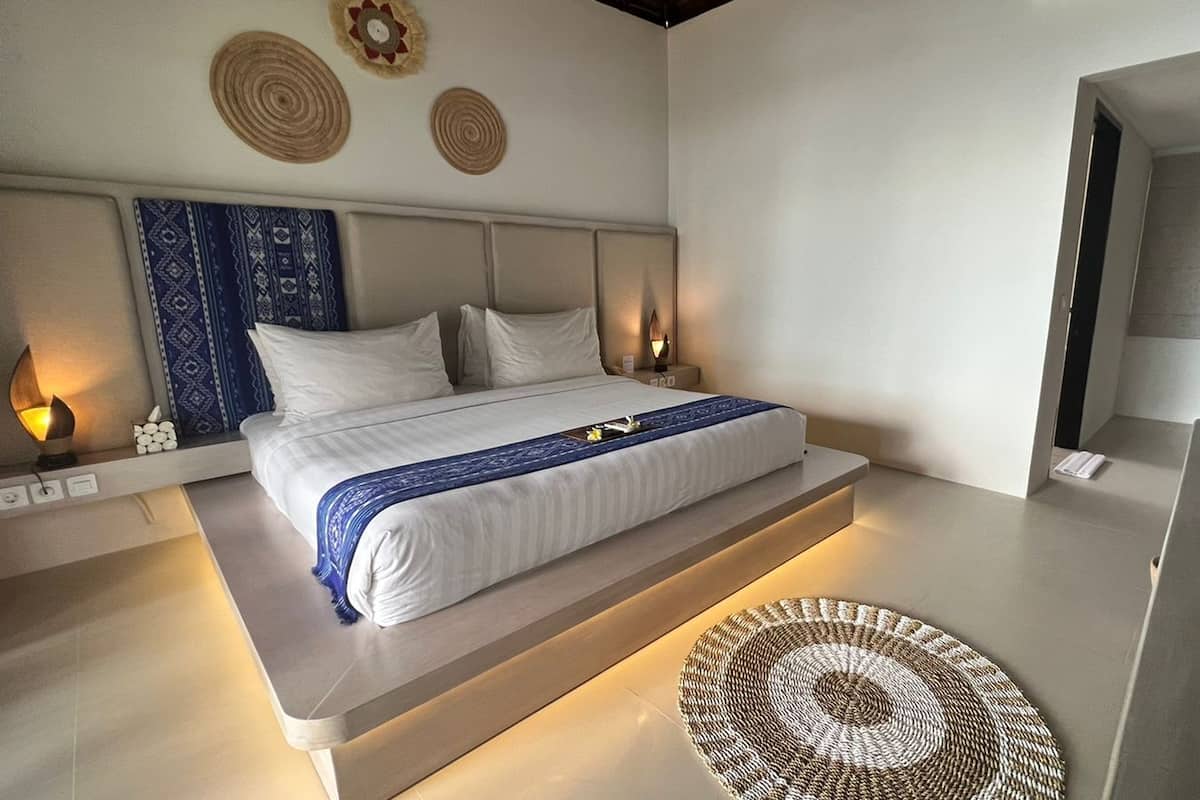 A modern bedroom with a large bed, bedside lamps, and a woven rug.