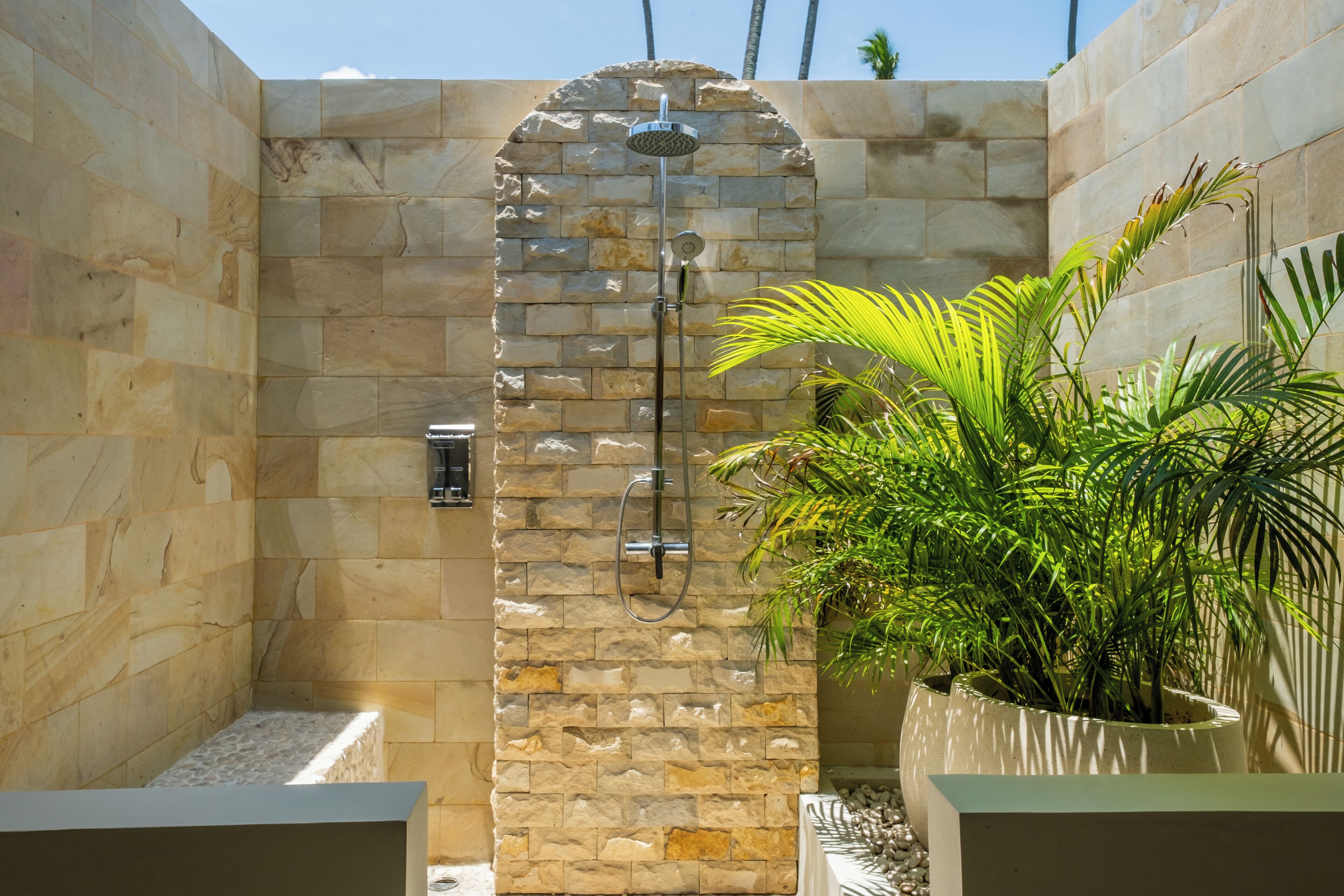 A stone-walled shower area with a rain showerhead, a handheld showerhead, and a handheld showerhead.
