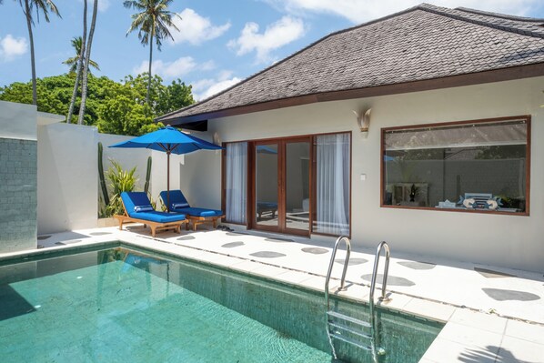 A poolside area with a clear pool, blue lounge chairs, and a blue umbrella.