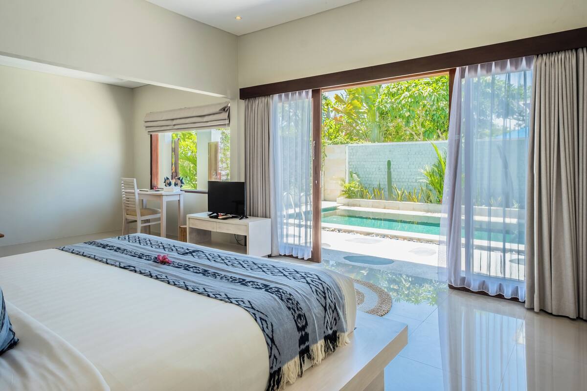 A bedroom with a large bed, a desk with a computer, and a view of an outdoor swimming pool.