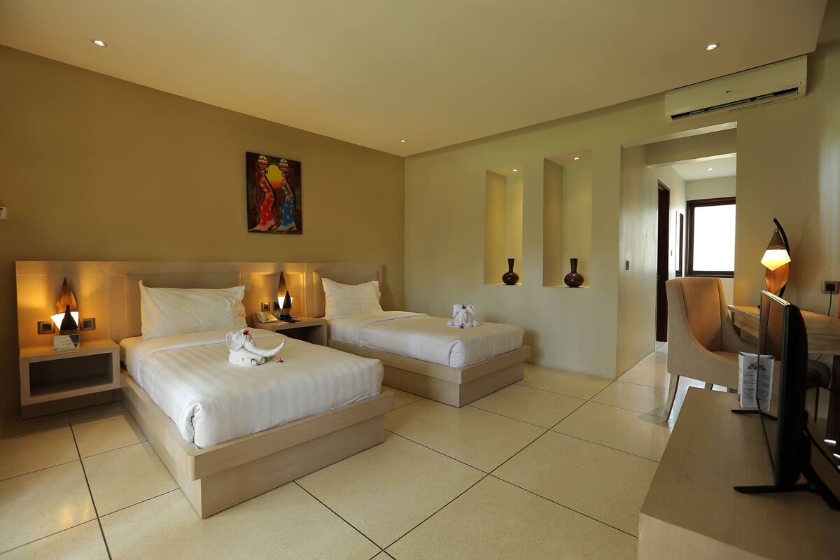 A hotel room with two beds, a desk with a computer, and a painting on the wall.