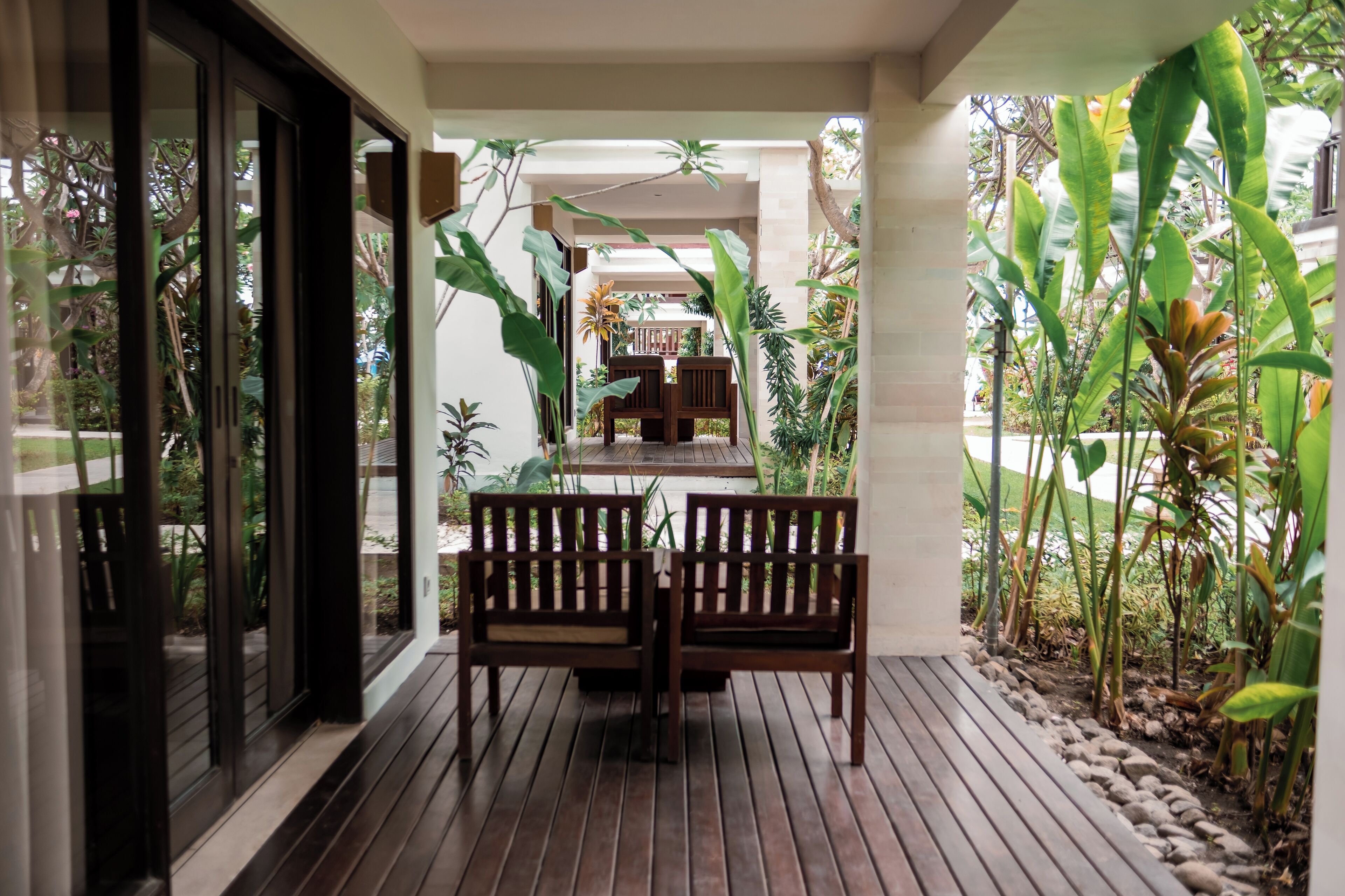 Una terraza de madera con dos bancos, rodeada de plantas tropicales y vistas a un jardín.
