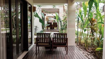 A wooden deck with two benches, surrounded by tropical plants and a view of a garden.