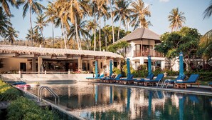 A pool area with lounge chairs, a thatched-roof structure, and palm trees. - Living Asia Resort & Spa (Senggigi)