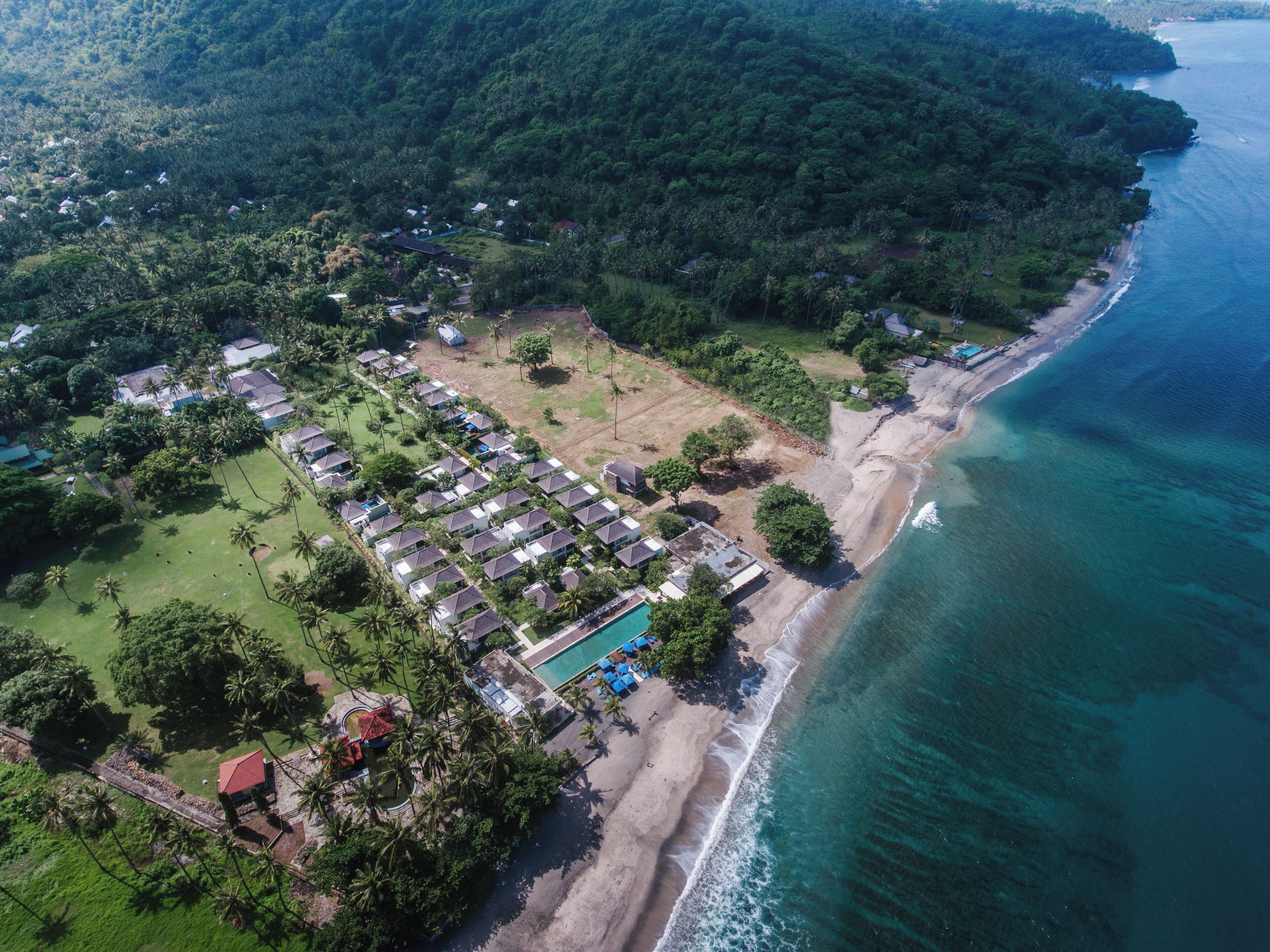 Vue aérienne d’un complexe hôtelier situé sur la côte, comprenant plusieurs hébergements de type bungalow, un espace piscine central et une plage donnant sur l’océan.