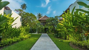 A pathway leading to a building with a thatched roof, surrounded by lush greenery and palm trees. - Living Asia Resort & Spa (Senggigi)