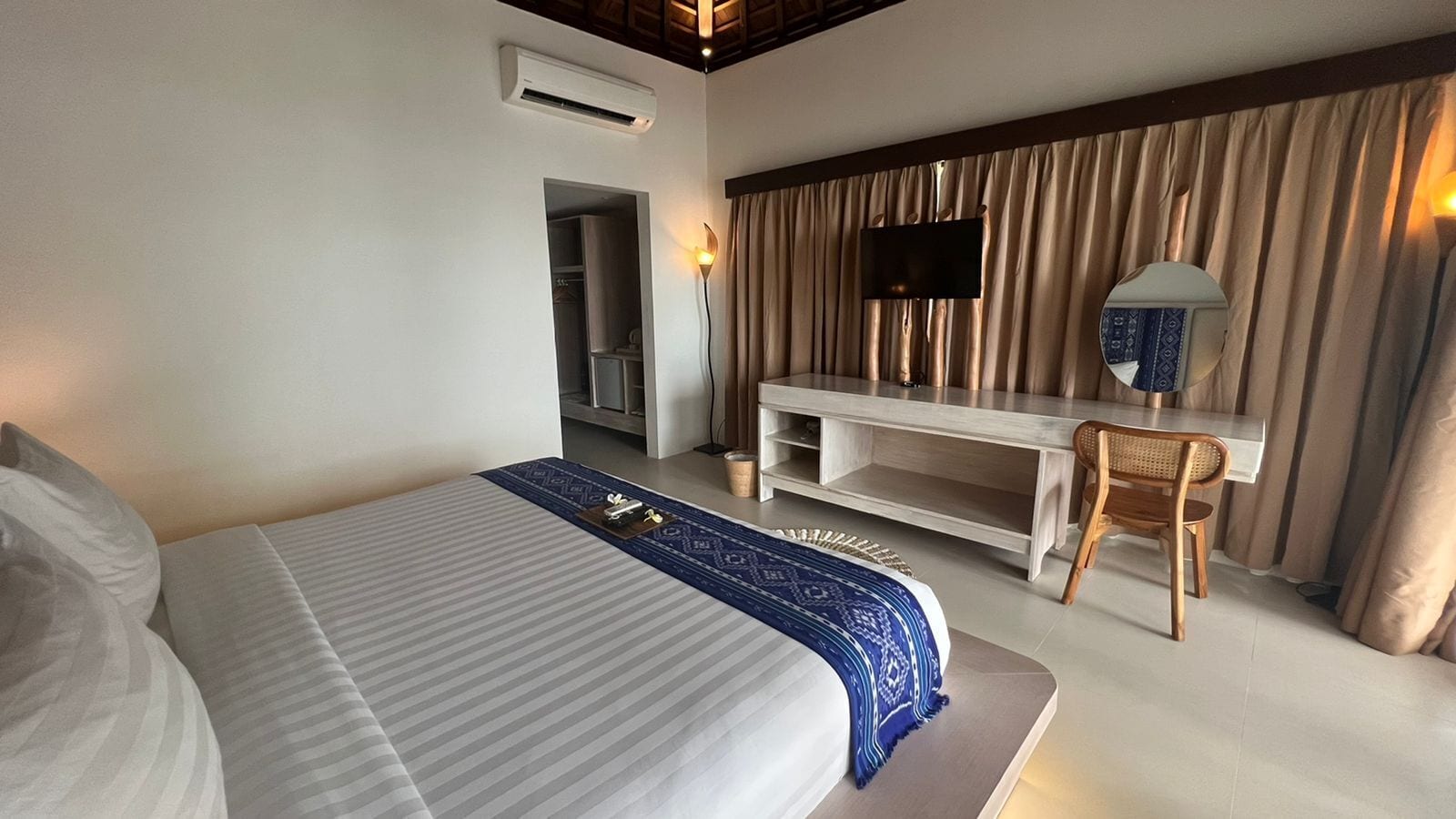 A hotel room with a large bed, a desk with a chair, a television, and a wardrobe.