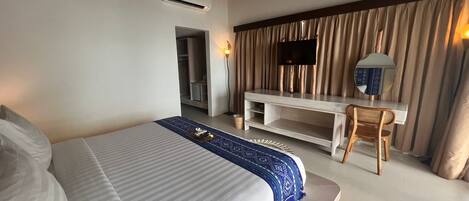 A hotel room with a large bed, a desk with a chair, a television, and a wardrobe.