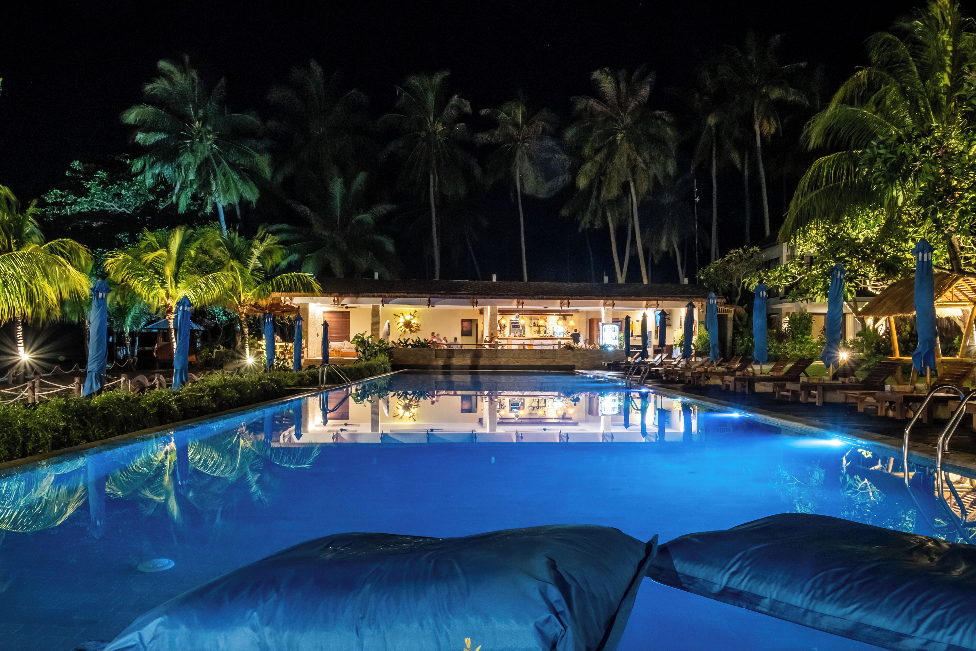 Ein Blick auf ein Schwimmbecken bei Nacht, mit Palmen und einem Gebäude im Hintergrund.