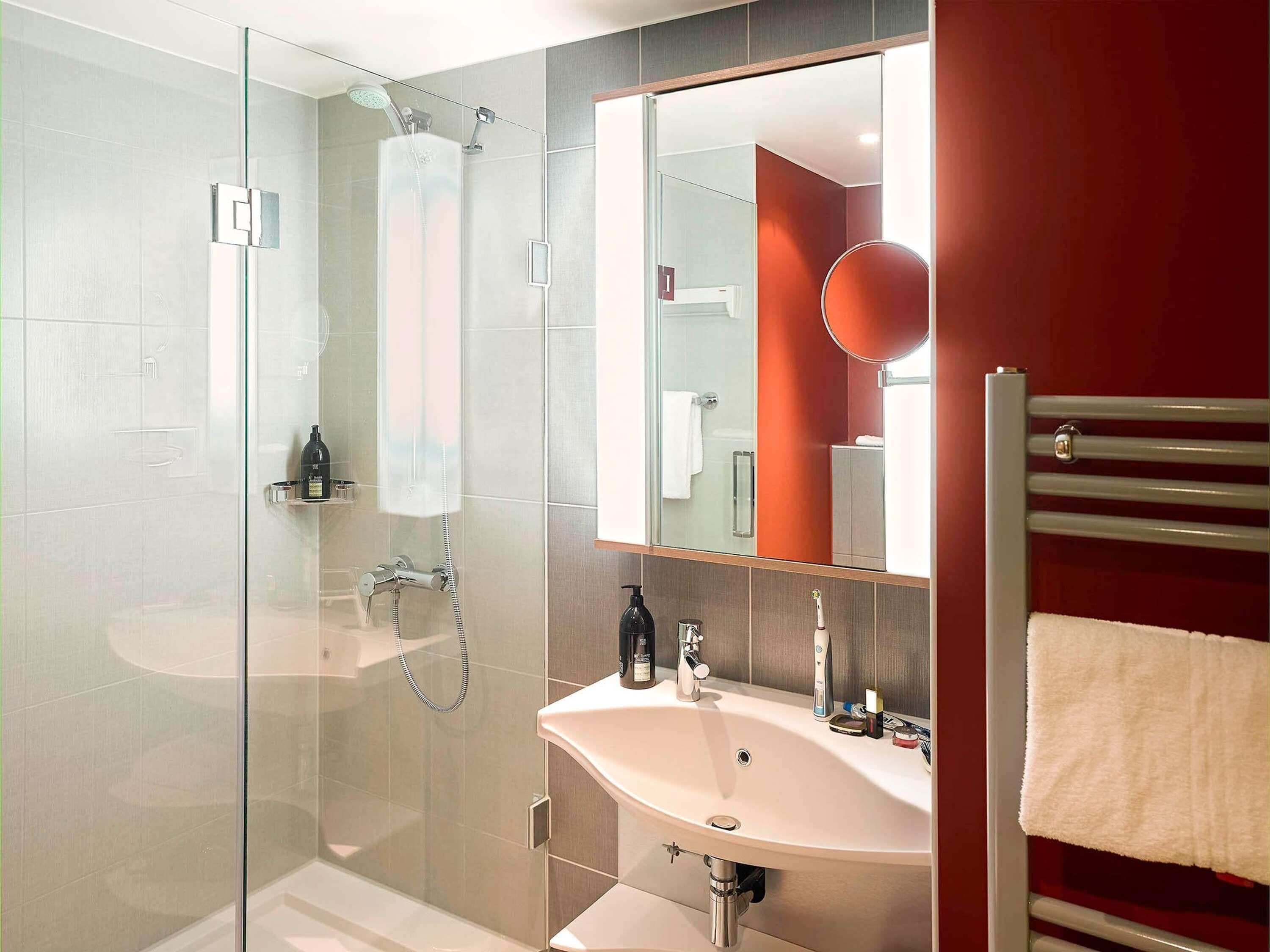 A modern bathroom with a glass-enclosed shower, a white sink, and a large mirror.