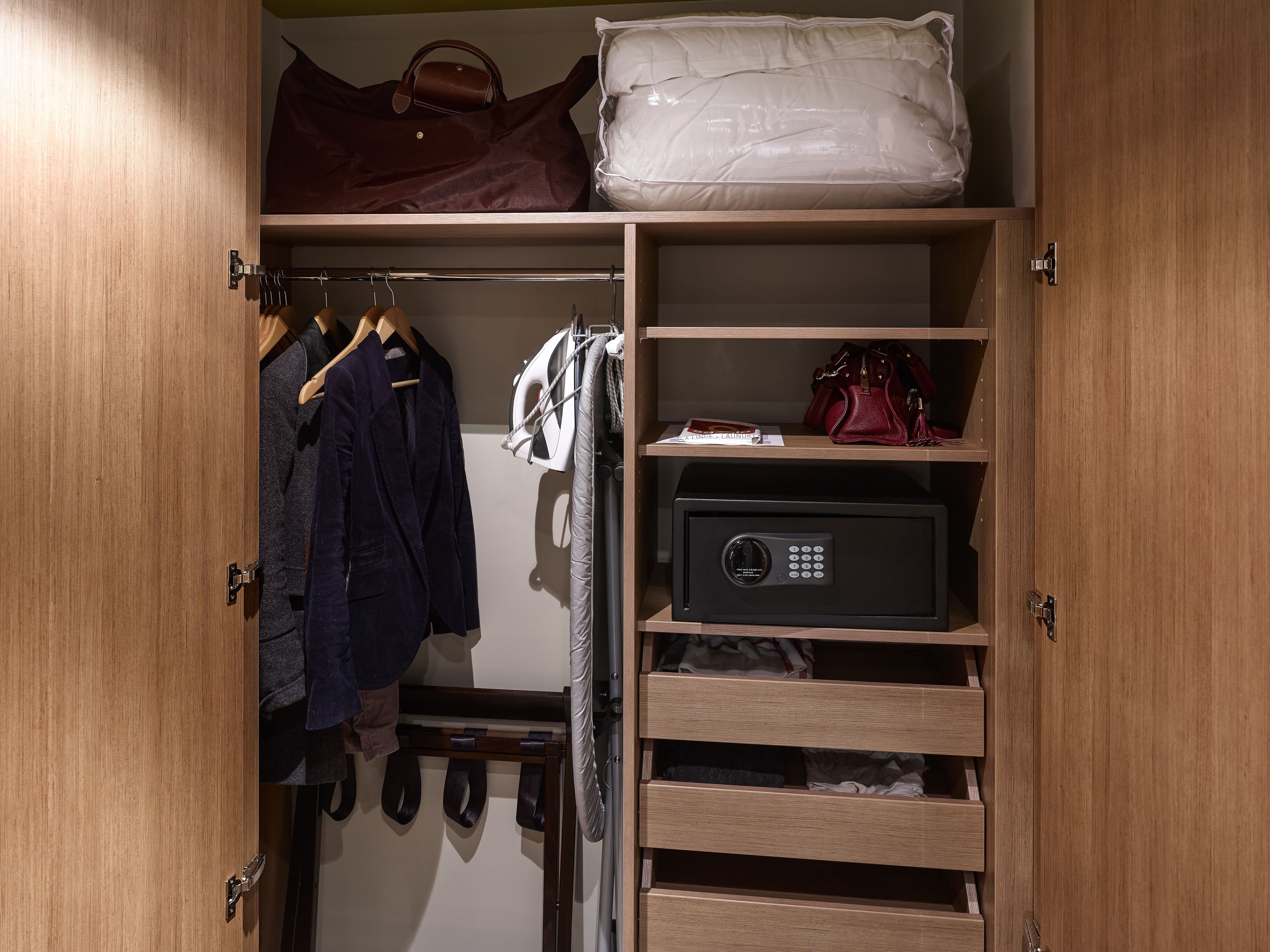 Une armoire en bois contenant des vêtements suspendus, un coffre-fort et une étagère avec des sacs.