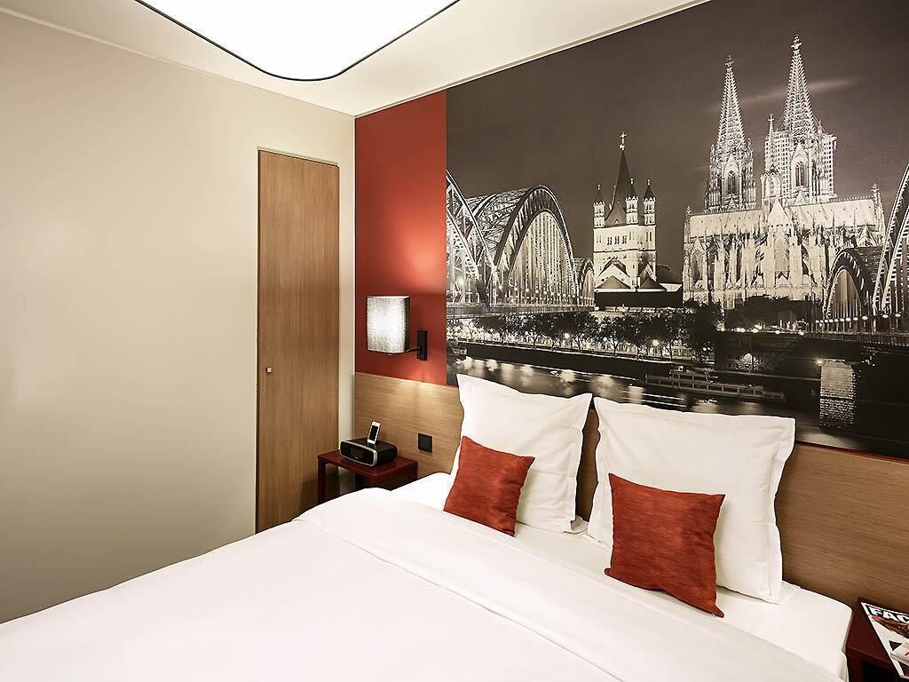 A hotel room with a large bed, a nightstand, a wall-mounted phone, and a cityscape poster.