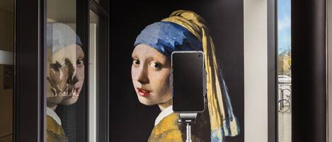 Un pasillo con un mural de una mujer con pañuelo amarillo y azul, un palo para selfies y una bicicleta al fondo.