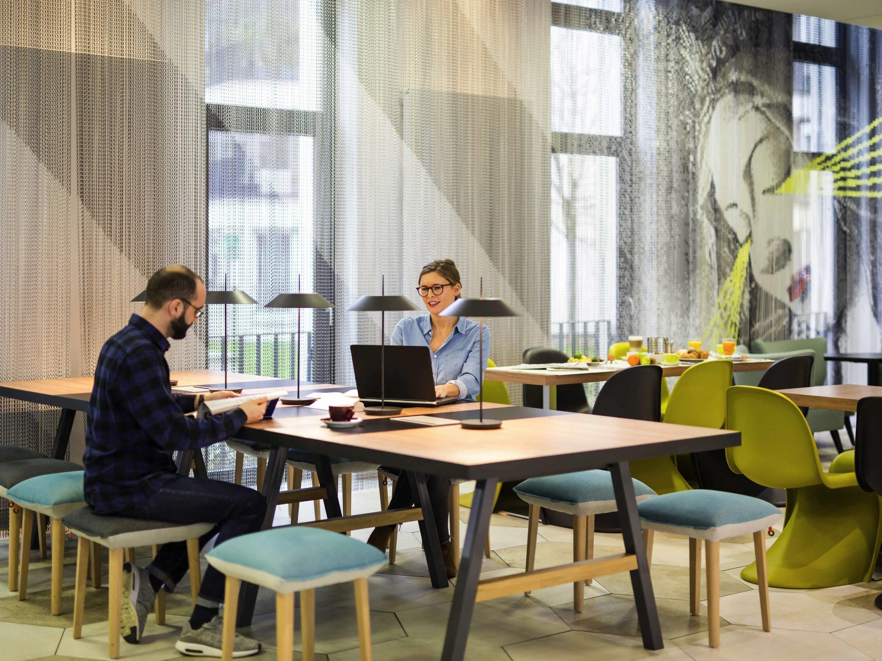 Ein moderner Büroraum mit mehreren Tischen, Stühlen, Laptops und einem großen Fenster mit Blick.