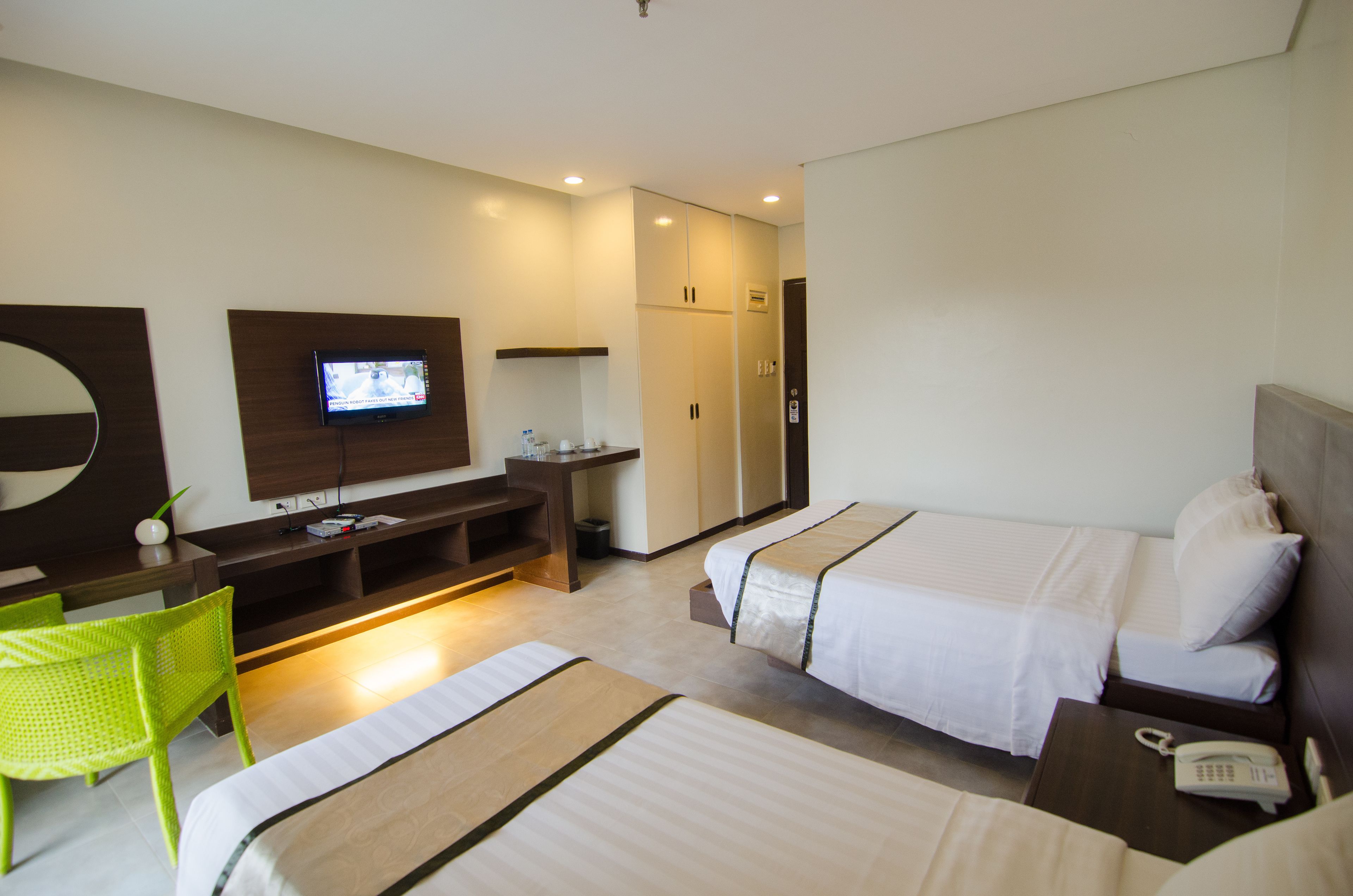 A hotel room with two beds, a TV, a desk, and a green chair.