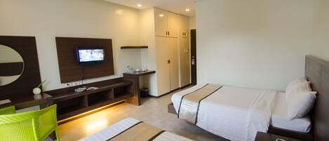 A hotel room with two beds, a TV, a desk, and a green chair.