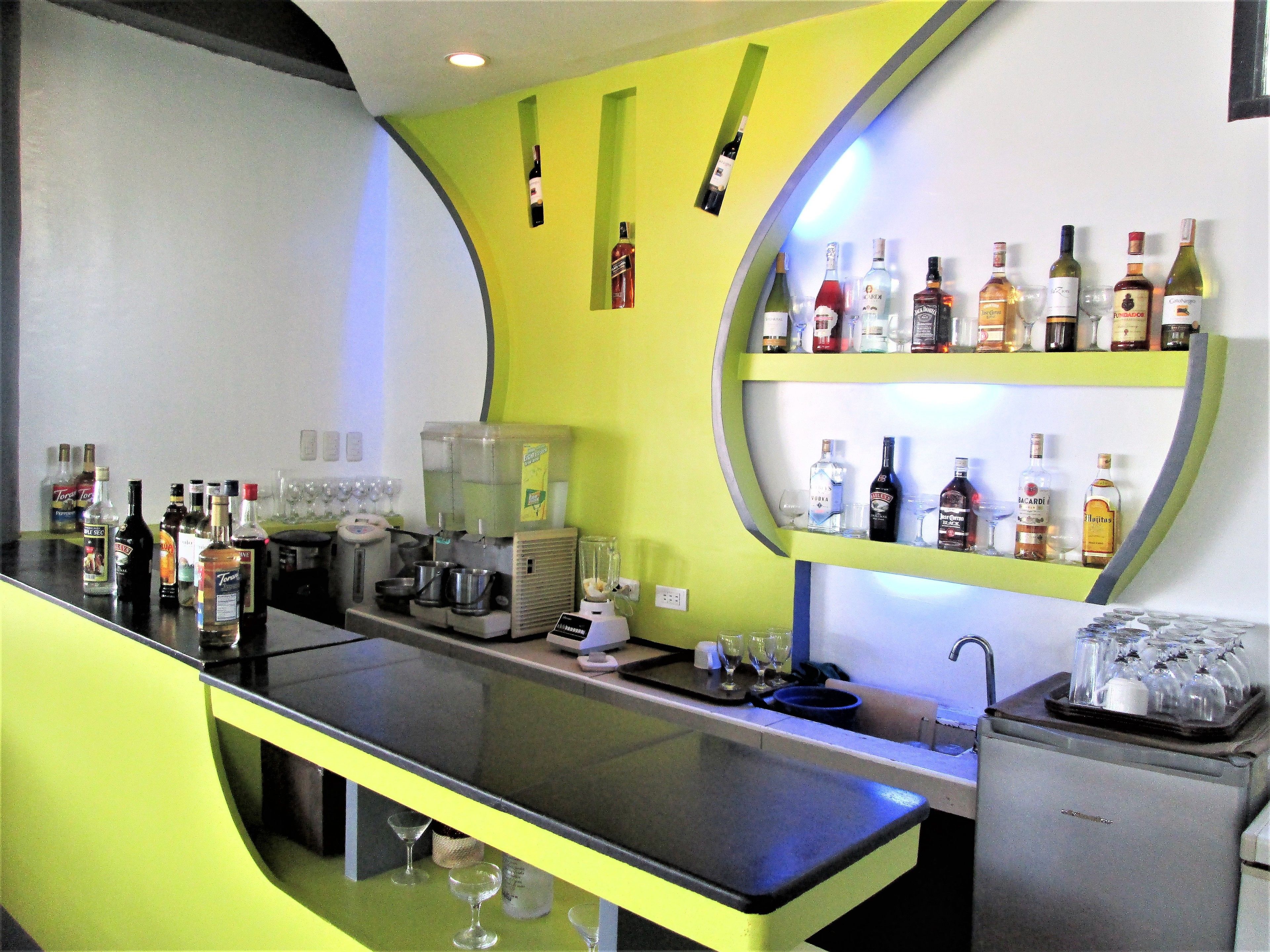 Zona de bar con estanterías llenas de botellas de licor, una máquina de café y un dispensador de agua.