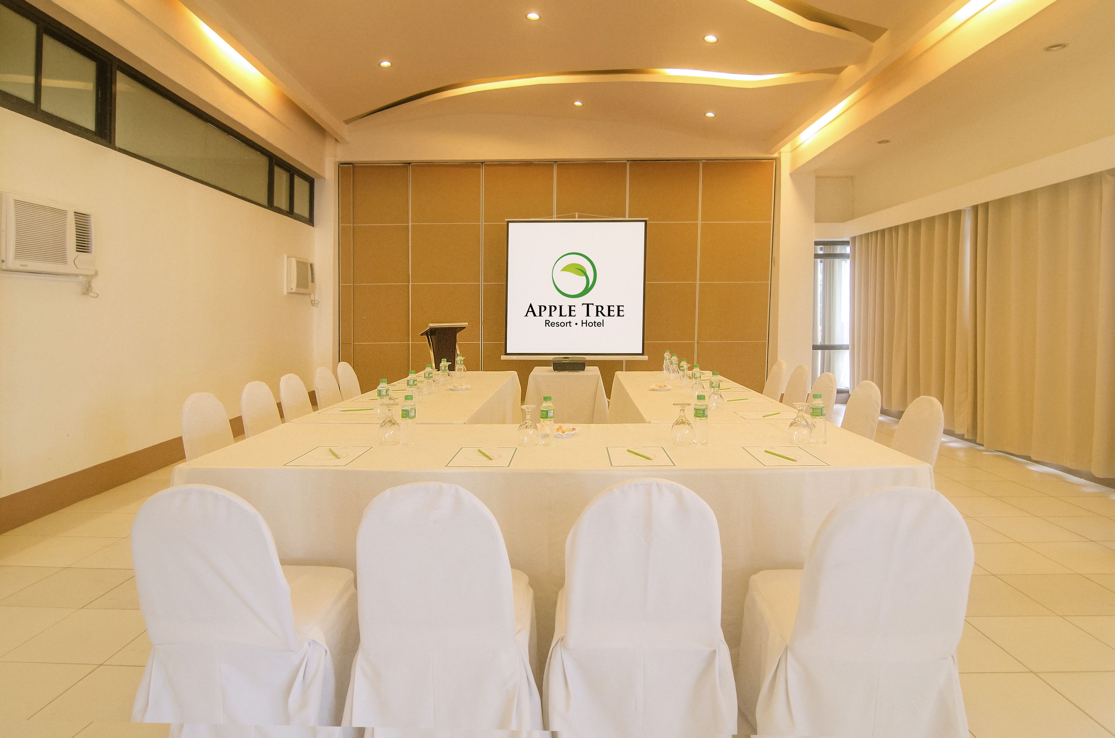 A conference room with a long table set for a meeting, white chairs, and a banner displaying the Apple Tree Resort Hotel logo.