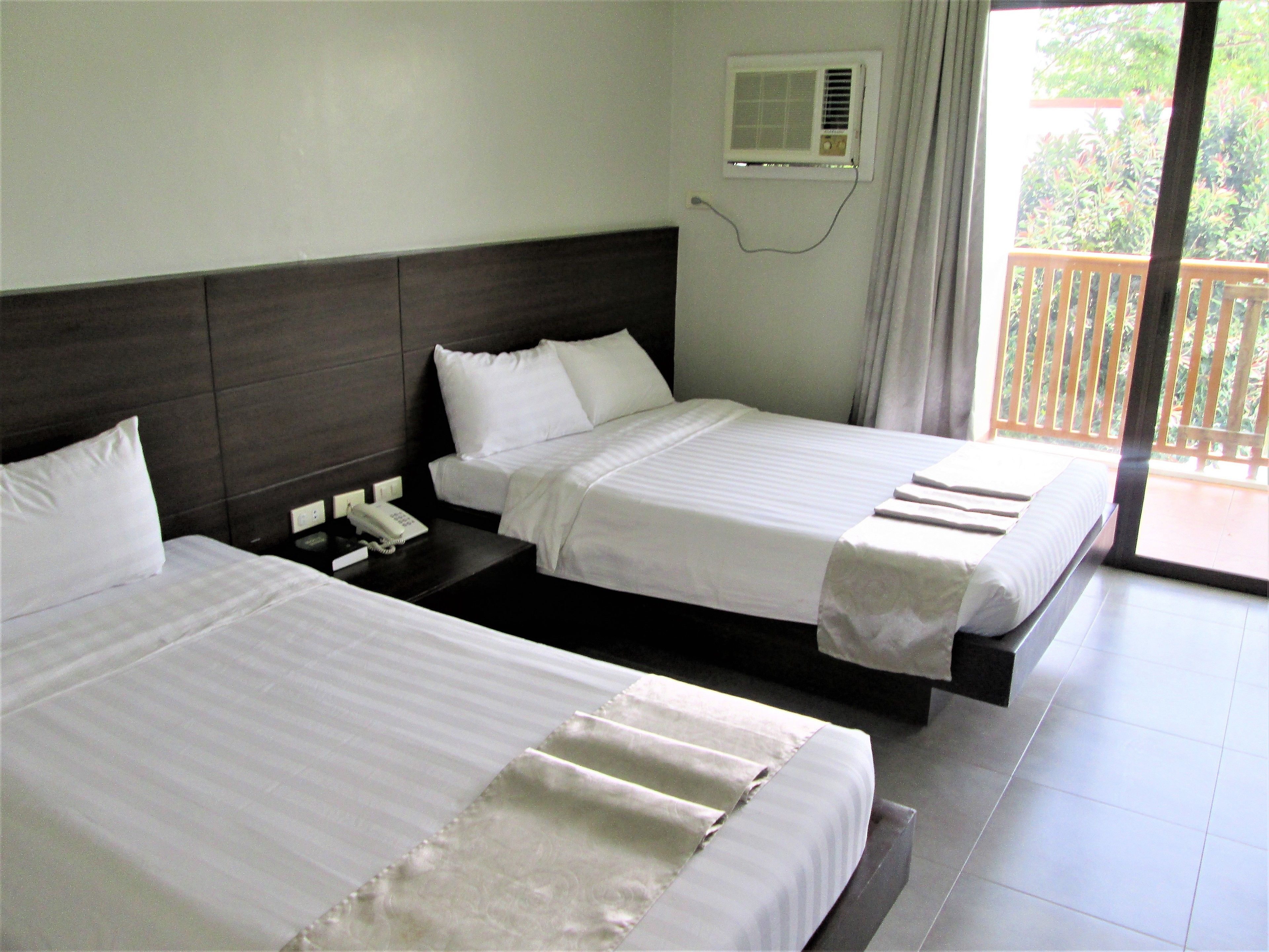 A hotel room with two beds, a bedside telephone, and an air conditioning unit on the wall.