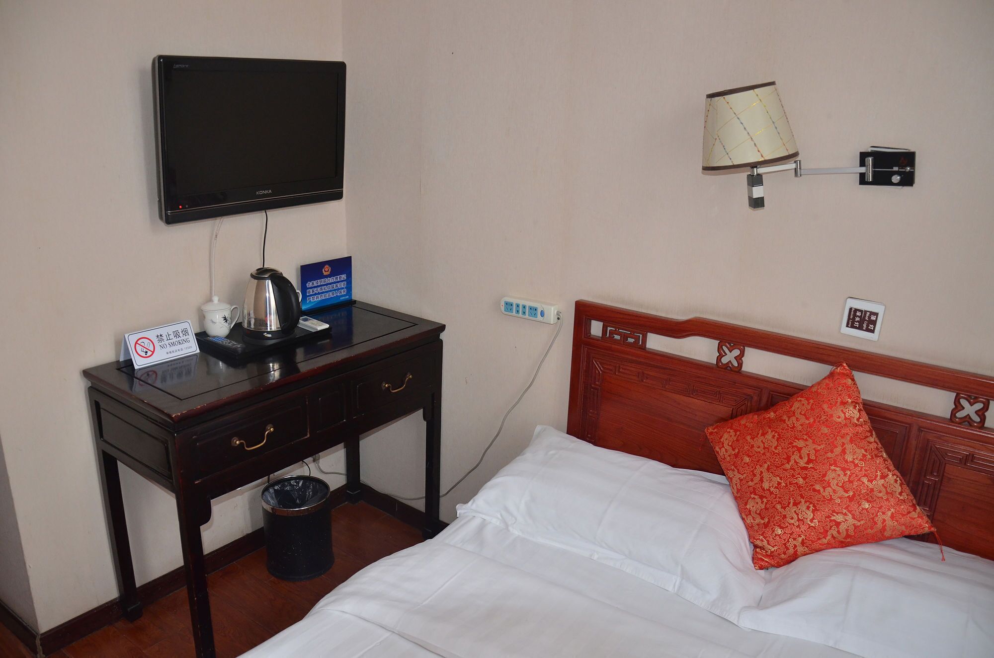 Une chambre d’hôtel équipée d’un lit, d’un bureau avec une télévision, d’une lampe et d’un panneau indiquant qu’il est interdit de fumer.