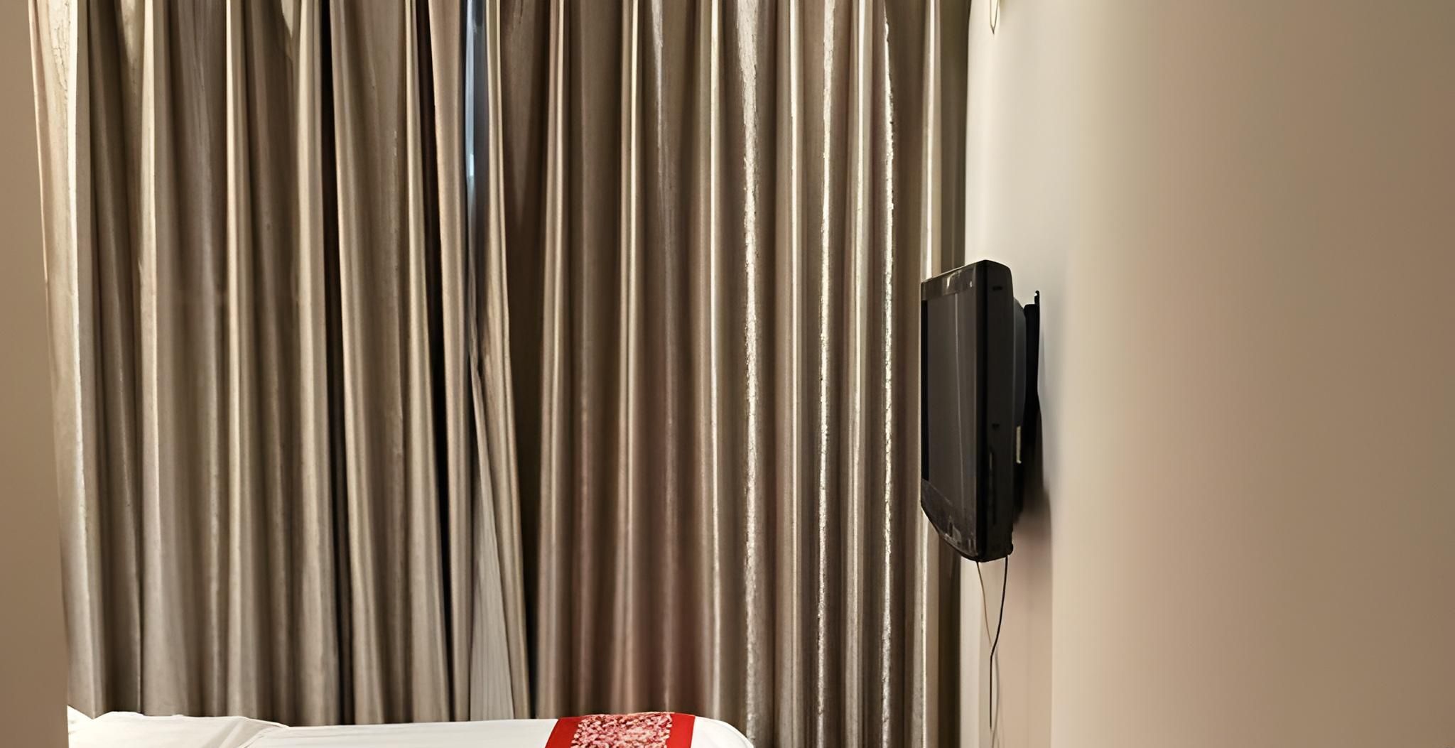 A hotel room with a bed, a TV mounted on the wall, and a curtain.