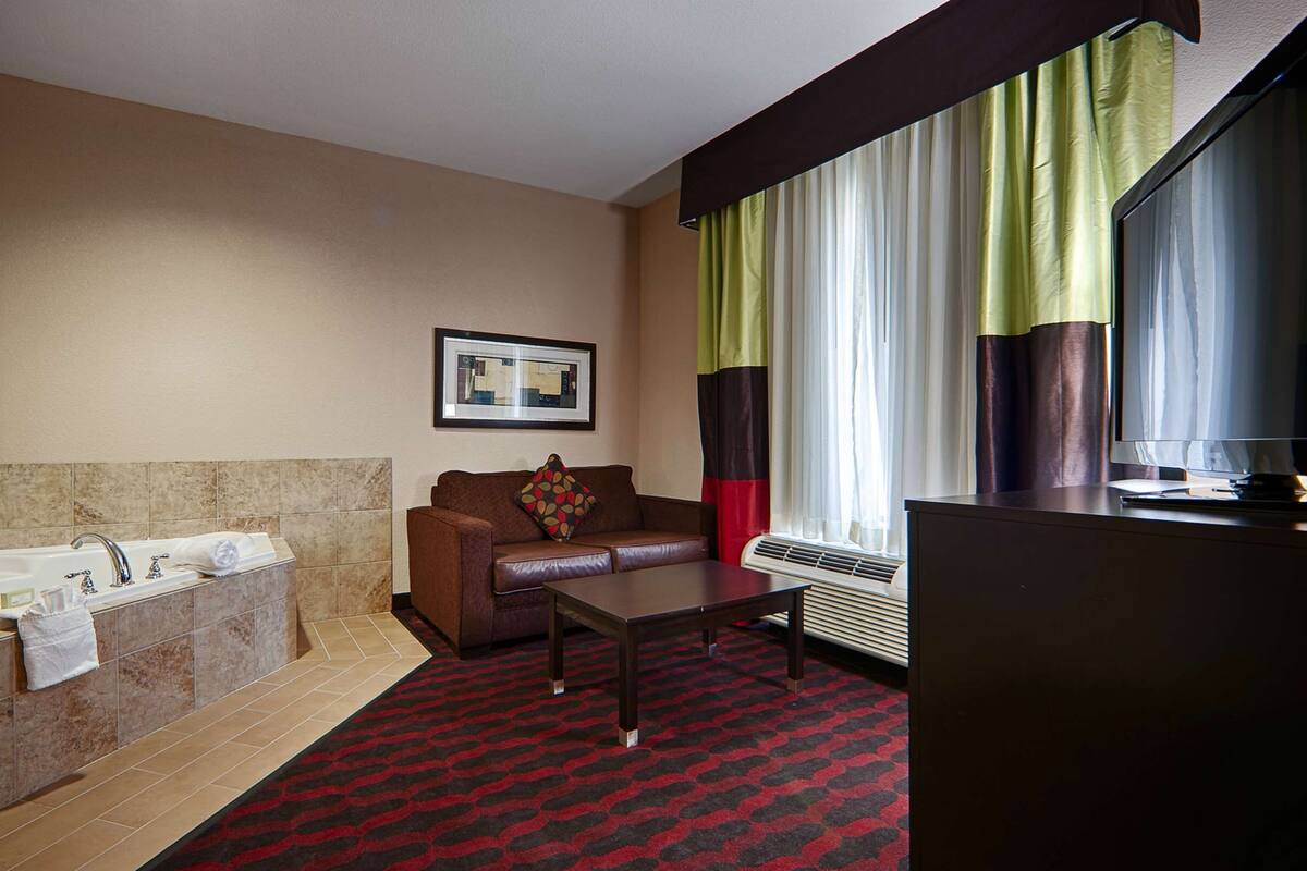 A hotel bathroom with a bathtub, a sofa, a coffee table, and a television.