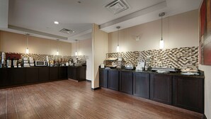 A modern hotel kitchen with dark wood cabinets, a tiled backsplash, and various appliances. - Best Western Plus Cushing Inn & Suites (Cushing)