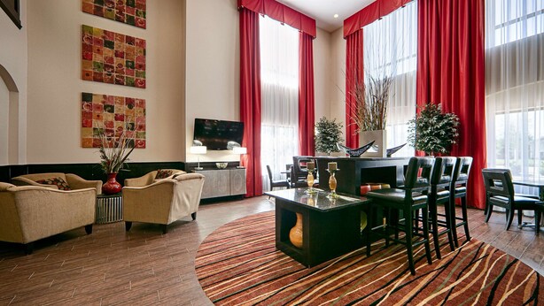 A hotel lobby with a seating area, a TV, and large windows with red curtains. - Best Western Plus Cushing Inn & Suites (Cushing)